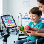A therapist supports a child during rehabilitation as the child uses a speech-generating communication device in a modern clinic.
